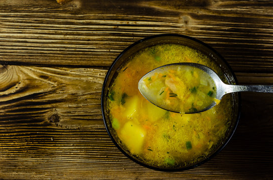 Vegetable soup in a glass bowl on wooden table. Spoon with soup. Top view