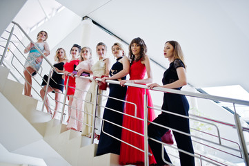 Group of outstandingly beautiful ladies in dresses posing on the stairs.