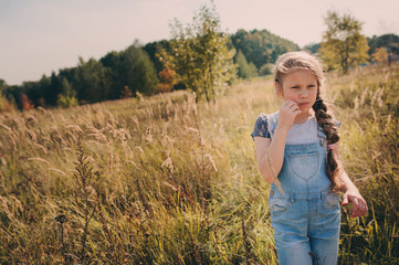 happy child girl in jeans overall playing on sunny field, summer outdoor lifestyle, cozy mood