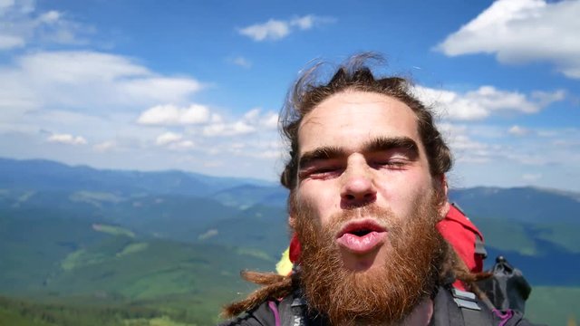 A man does selfie in the mountains. Joyous video, turn in a circle.