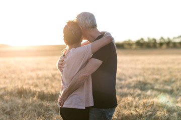 Senior couple embracing each other in a wheat field, sunlight effect