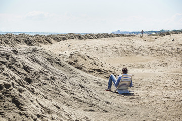 back view of a y man reading a book on the beach