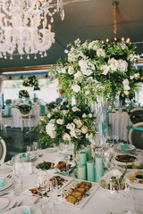 Rich bouquet of white roses and greenery stands in the middle of dinner table