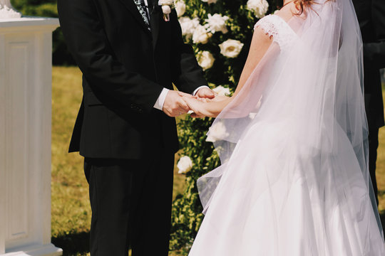 Groom holds bride's hand tender standing before an altar