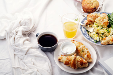 Breakfast in bed. Scrambled eggs with cheese croissants, raspberry muffin and black coffee. Morning treat concept. Side view with copy space.