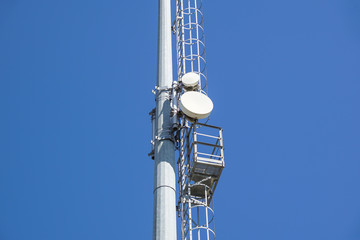 Outdoor stadium lights and telecommunication tower against daytime blue sky.
