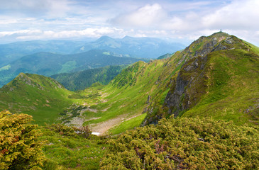 Valley among majestic green and rocky mountain hills covered in green lush grass, bushes with a Pip Ivan peak. Sunny cloudy day in summer in June. Maramures, Carpathian mountains, Ukraine