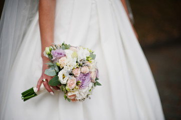 Close-up photo of bride holding a bouquet in her hand outdoor.