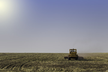 Tractor ploughing a field with a trail of dust behind it