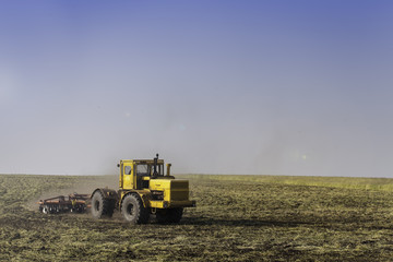 Fototapeta premium Tractor ploughing a field with a trail of dust behind it