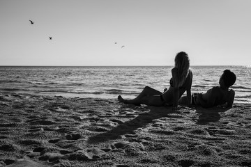 Young couple lying on the beach and looking at the flying birds in the sky in summer evening. 