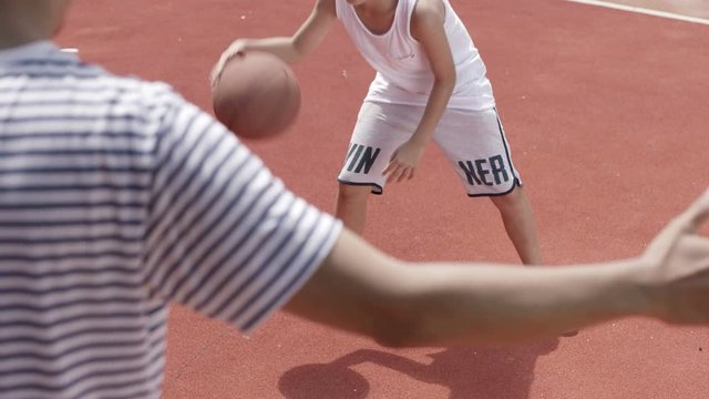 over shoulder shot of Asian boy playing basketball in court in slow motion