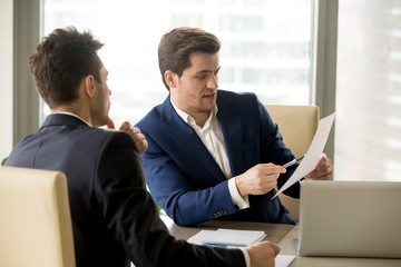 Two serious business partners discussing financial report, analyzing teamwork results, businessman...