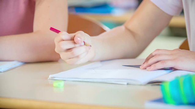 A young girl is writing something down into her notebook with a pencil. They are having a math class.