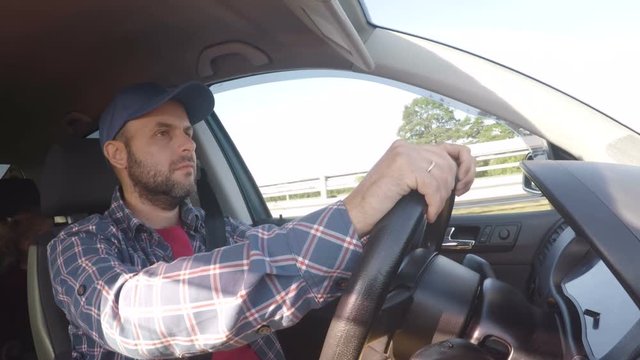 A man in a checked shirt and a baseball cap behind the wheel of a car. Man driving a car