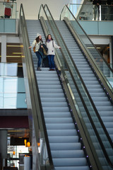 Two young women with small luggage on the escalator at the airport.