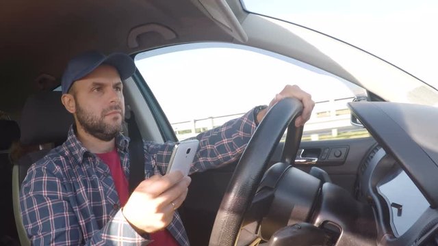 Man driving car on highway and texting on smartphone.  Man with mobile telephone, driver with cell phone, driving car on street, using smartphone text messaging and internet. Danger and risk on road