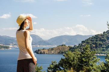 Young beautiful smiling woman in a hat on a high mountain looking at the sea