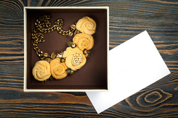 Peach-colored handmade necklace putted in a box and a letter of congratulations are lying on wooden background