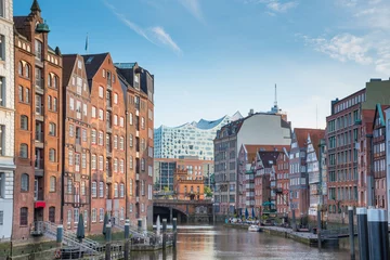 scenic view of historic buildings on both sides of Nikolaifleet channel in Hamburg, Germany with Elbphilharmonie concert hall in background under beautiful summer sky © Christian Horz