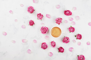 Morning coffee cup, petals and beautiful pink rose flowers on white stone table top view in flat lay style. Cozy breakfast on Mother or Woman day.