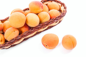 Several of harvested apricots in basket with whole and halved apricots on white background..