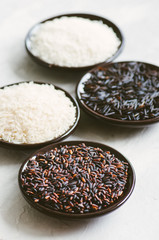 Set of various rice in plates on white stone background: black, basmati, brown and jasmine rice. Toned.