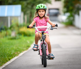 Children learning to drive a bicycle on a driveway outside.