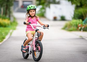 Children learning to drive a bicycle on a driveway outside.