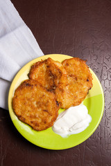 Potato pancakes with meat and sour cream on green plate in Belarusian style on dark background.