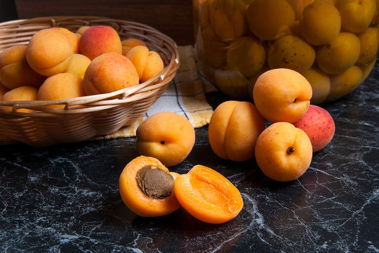 Fresh organic harvested apricots in basket and big glass jar with canned apricot compote on dark marble..