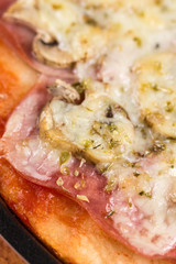 Baked pizza with ham mushrooms grated cheese oregano on the round baking pan on the table