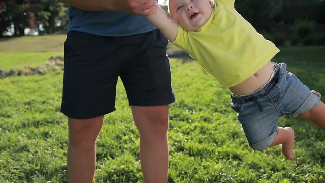 Man swinging his toddler baby boy by hands in park