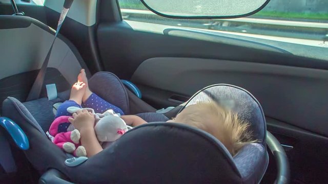 A girl is peacefully sleeping on a child safety seat when driving in a car on a highway. 