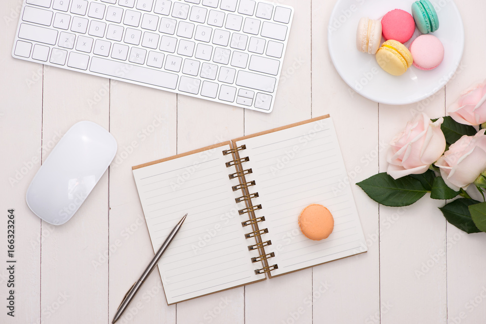 Poster white desk with colorful macaroons, keyboard and open notebook.