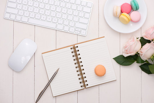 White desk with colorful macaroons, keyboard and open notebook.