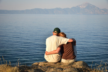 Couple in love sitting on the top of the hill in the sunset, hugging and enjoying the view