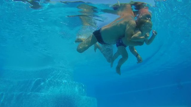 Father and son are dipping under water in the swimming pool