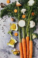 Raw vegetables and bouillon cubes for cooking soup. Young carrot with haulm, broccoli, cauliflower, onion, garlic, salt pepper over gray concrete background. Top view. Dinner cooking concept