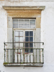 old picturesque crumbling balcony window with peeling white paint and a rusting green railing and cracked wooden frame in the algarve region of portugal
