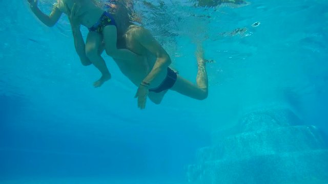 Father and son are dipping under water in the swimming pool