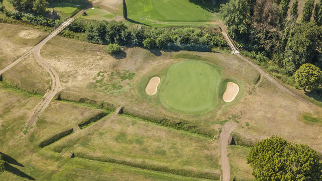 Vista aerea di un campo da golf vuoto con colline verdi e dune di sabbia. Il circolo sportivo è curato e ricco di alberi e vegetazione.