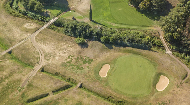 Vista aerea di un campo da golf vuoto con colline verdi e dune di sabbia. Il circolo sportivo è curato e ricco di alberi e vegetazione.