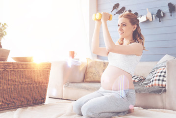Obraz na płótnie Canvas Positive beautiful pregnant woman doing sport exercises