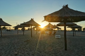 The panorama of the beach by the sea with the straw umbrellas against the sunset