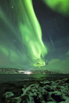 Northern lights, aurora borealis, above a fjord surrounded by a village and mountains in Troms county Norway.