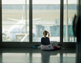 The little girl sits near a big window at the airport.