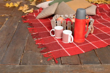 Autumn picnic on the terrace. Red plaid, basket with apples and thermos with hot drink. Veranda of countryside house in autumn season.