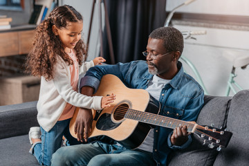 man playing guitar with daughter at home