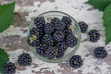 Close up of a cup of ripe blackberries placed on a white rustic table in the garden. Shallow depth of focus. Health concept from nature.